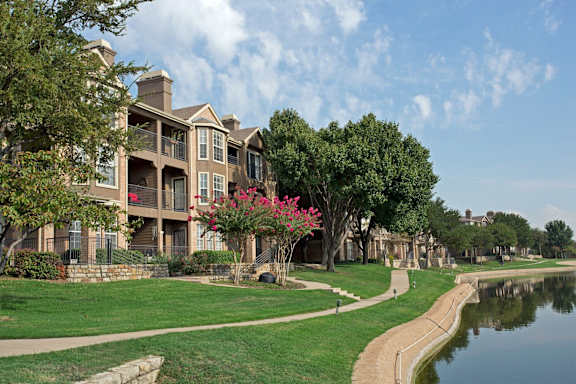 A large building with a balcony is surrounded by a grassy area and a body of water.