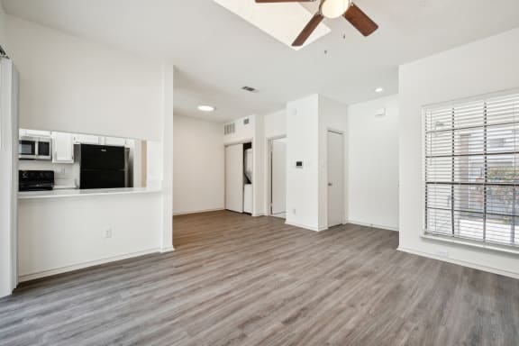 an empty living room with a ceiling fan and a kitchen