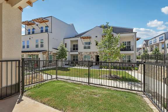 A black iron fence surrounds a grassy area in front of a white building.