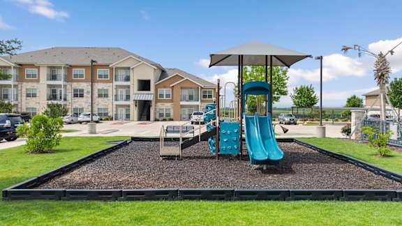 A playground with a blue slide and a brown building in the background.