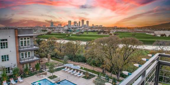 A beautiful sunset view from a balcony overlooking a pool and a city skyline.