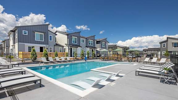 A swimming pool surrounded by lounge chairs and apartment buildings.