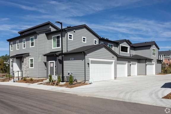 A modern two-story house with a grey exterior and white garage doors.
