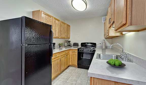 A black refrigerator is in a kitchen with wooden cabinets.