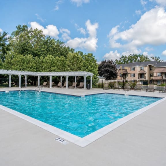 A large swimming pool with a white pergola and lounge chairs.