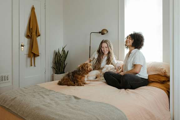 Two women sitting on a bed with a dog.