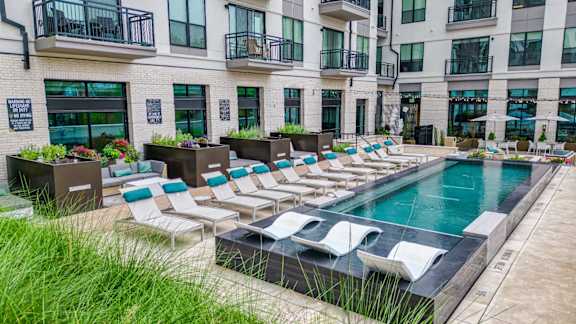 A pool surrounded by lounge chairs and greenery.