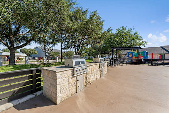 A stone barbecue grill is in the middle of a sandy area.