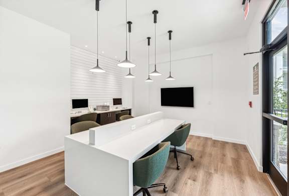 A white desk with green chairs and hanging lights in a room.