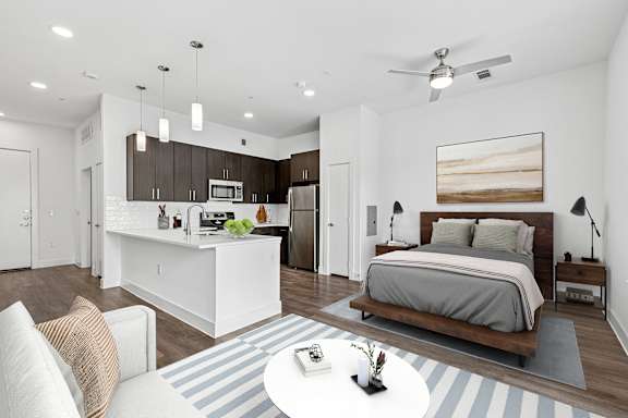 A modern bedroom with a large bed and a kitchen area in the background.