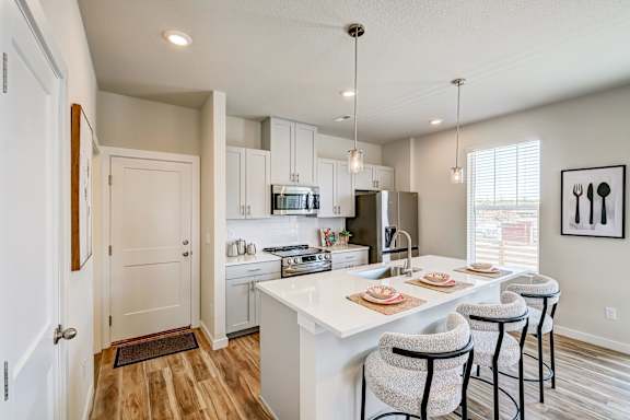 A kitchen with white cabinets and a white island with three barstools.