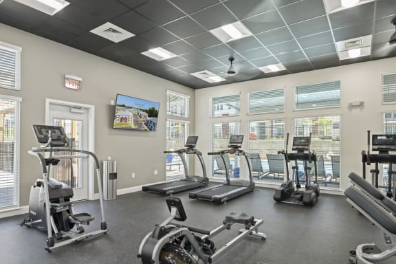 a gym with cardio machines and windows and a tv