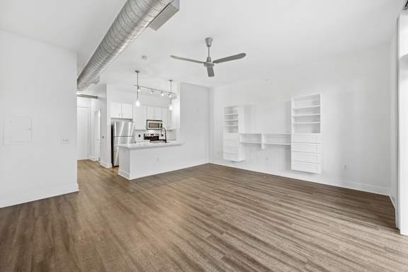 A room with a ceiling fan and a kitchen area in the background.