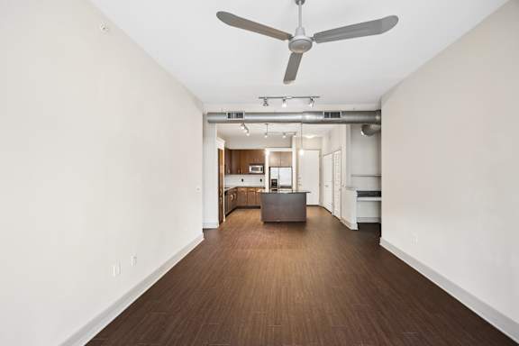 A room with a ceiling fan and a long wooden floor.