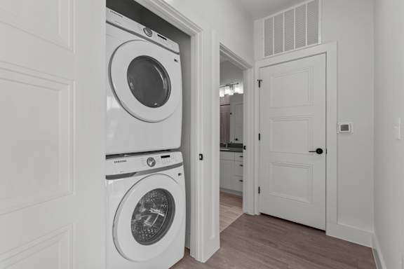 A white door is open to a hallway with a washer and dryer stacked on top of each other.