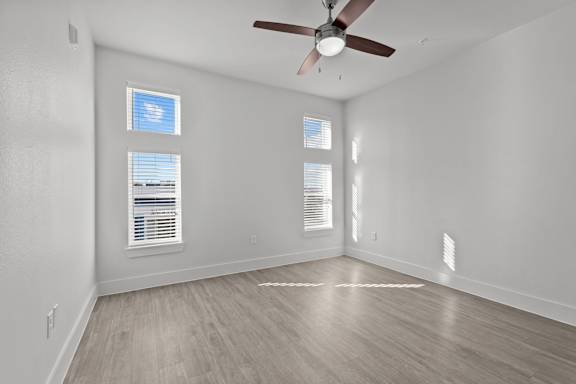 A room with a ceiling fan and three windows.