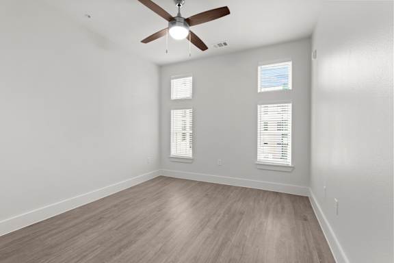 A room with a ceiling fan and two windows.
