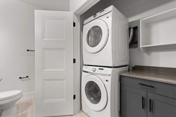 A white door is open to reveal a stack of white washing machines.