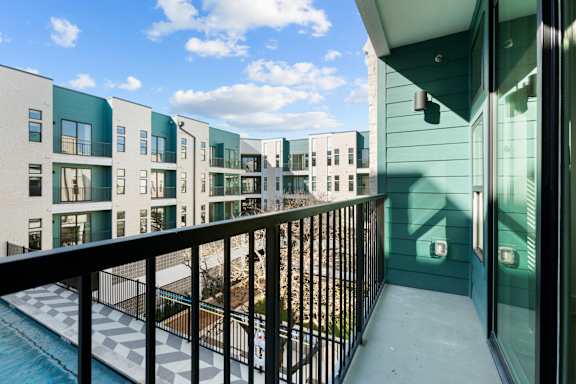 A balcony with a black railing overlooks a pool and apartment buildings.