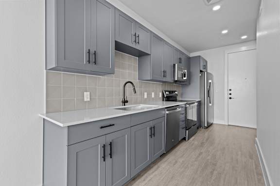 A modern kitchen with grey cabinets and a white countertop.