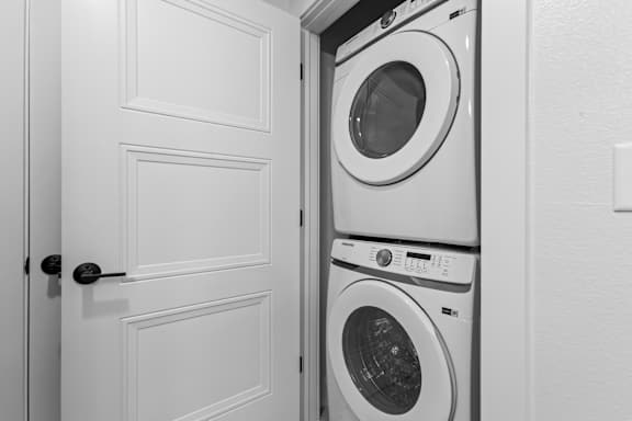 A white door is open to a stack of white washing machines.