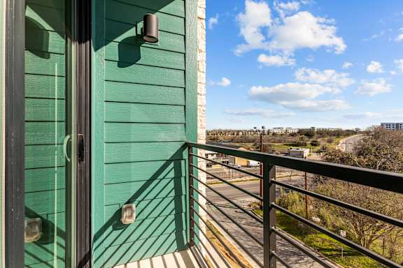 A balcony with a green wall and a metal railing overlooking a street.