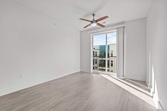 A room with a ceiling fan and a sliding glass door leading to a balcony.