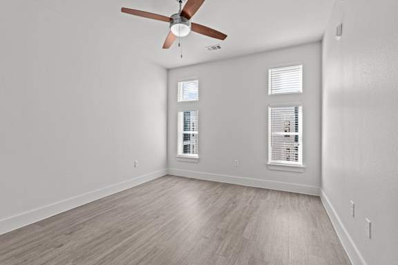 A room with a ceiling fan and two windows.