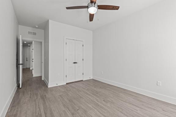 A room with a ceiling fan and light fixture, two doors, and a hallway leading to another room.