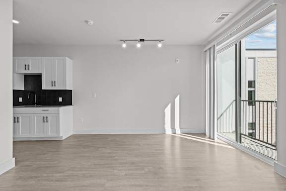 A spacious, empty room with a kitchen area to the left and a balcony to the right.