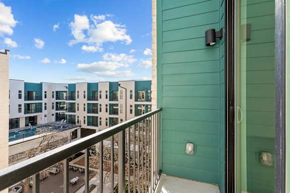A balcony with a green wall and a view of a parking lot and other buildings.