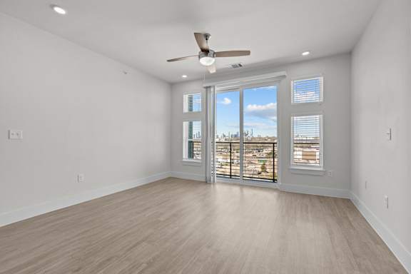 A spacious room with a ceiling fan and sliding glass doors leading to a balcony.