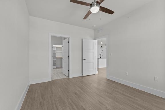 A room with a ceiling fan and light, two doors, and a wooden floor.
