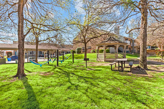 A playground with a swing set and a picnic table is surrounded by trees.