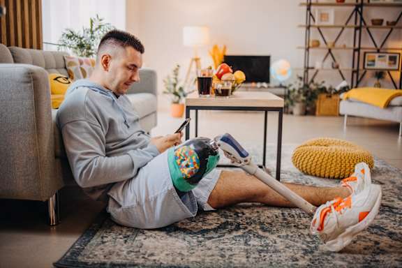 A man with a prosthetic leg is sitting on the floor in a living room.