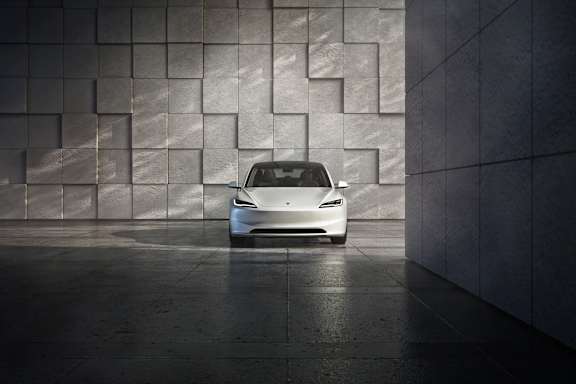 A white car is parked in front of a wall with a geometric pattern.