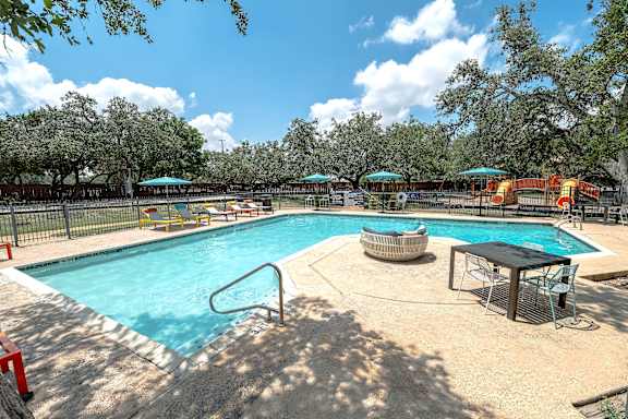 A large outdoor swimming pool surrounded by trees and a fence.