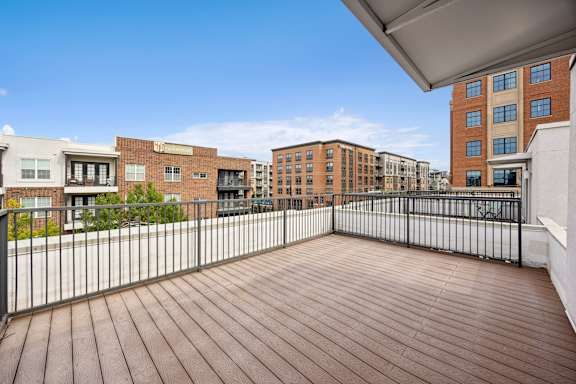 A wooden deck with a metal railing and buildings in the background.