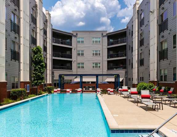 A swimming pool in front of a building with red lounge chairs.