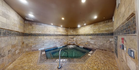 A hot tub in a stone-walled room with a brown floor.