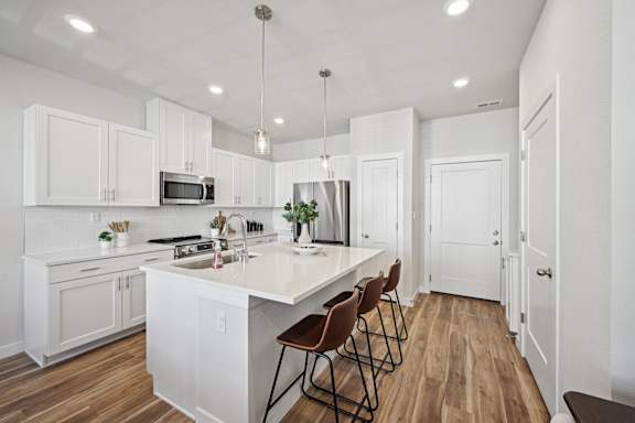 A kitchen with white cabinets and a white island with brown chairs.