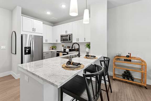 A kitchen with a marble countertop and black chairs.