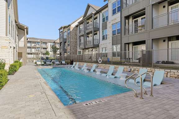 A pool surrounded by chairs and buildings.