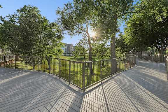 A sunny day at the park with a wooden walkway and metal fence.