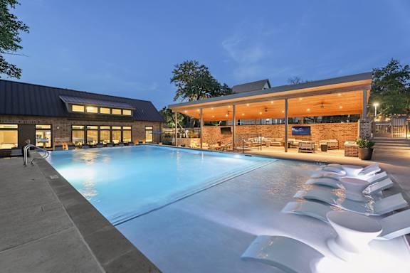 A large outdoor swimming pool with loungers and a building in the background.