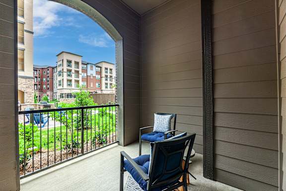 A balcony with a chair and a table overlooking a courtyard.
