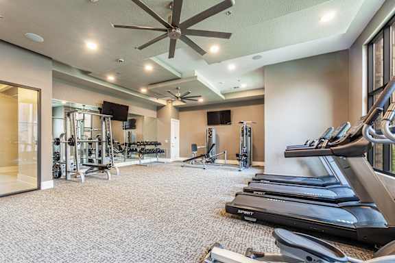 A spacious gym with treadmills, weights, and a ceiling fan.
