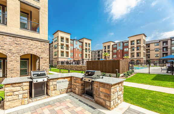 A BBQ area is surrounded by a brick wall and is located in a grassy area.