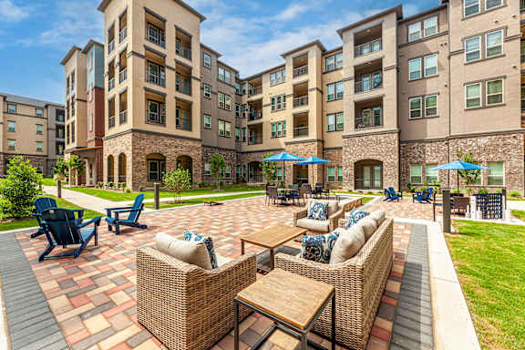 A sunny day at a courtyard with a brick floor and a seating area with wicker chairs and tables.