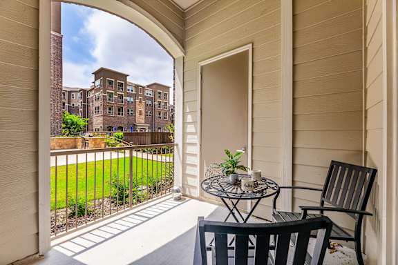 A patio with a table and chairs overlooks a green lawn and a brick building.